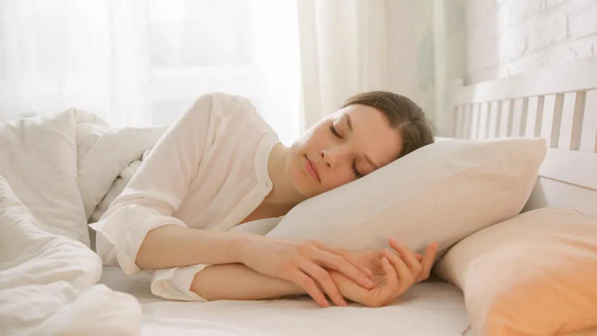 Mulher dormindo tranquilamente em uma cama confortável, ilustrando os benefícios do sono de qualidade para a saúde física e mental.