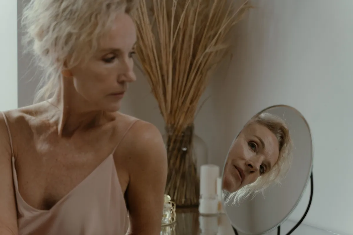 Mulher observando a pele no espelho, representando os benefícios do colágeno para a firmeza, elasticidade e saúde da pele.