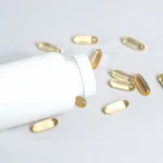 Suplemento de ômega 3 em cápsulas ao lado de um frasco branco, representando os benefícios do ômega 3 para a saúde do coração, cérebro e organismo.