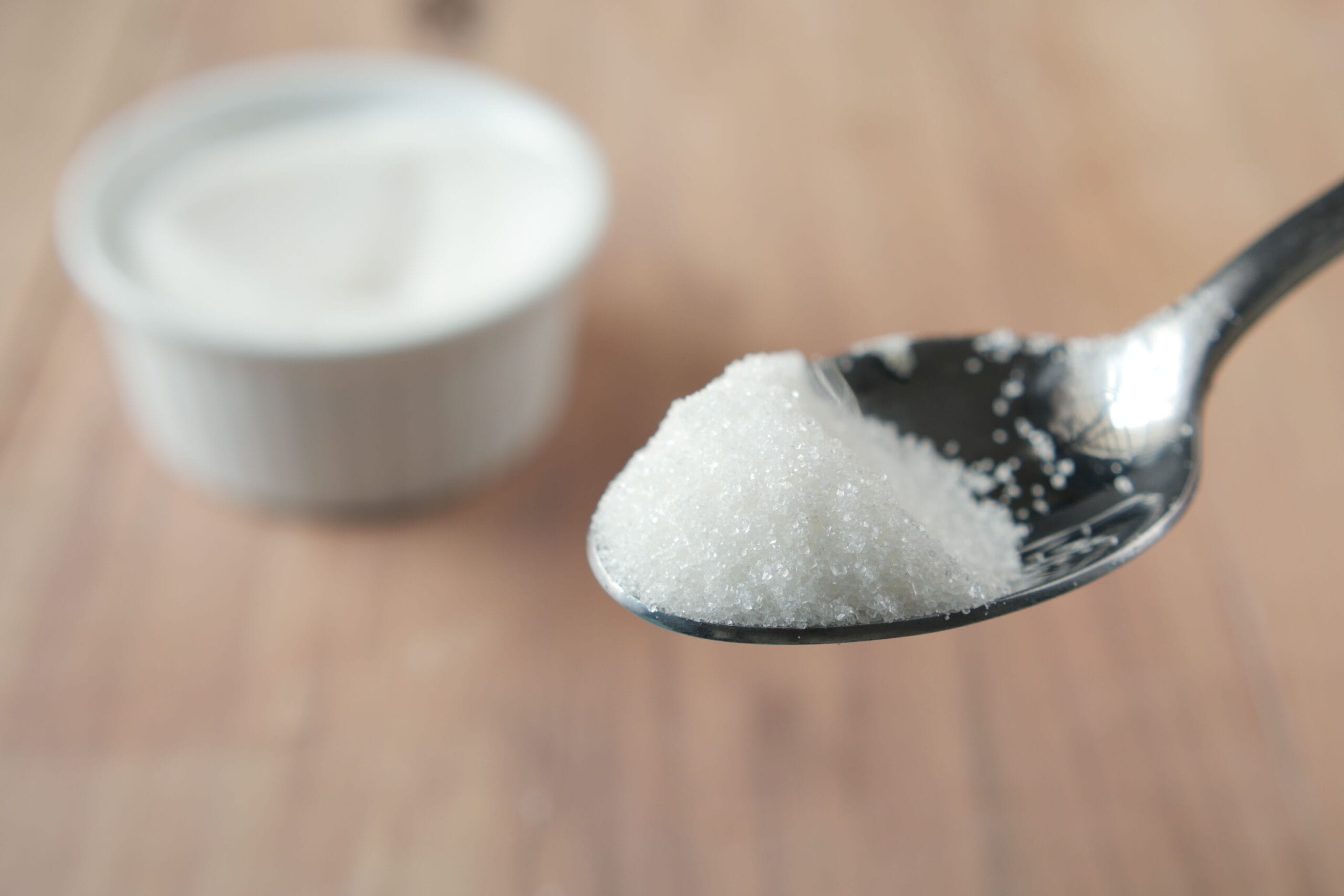 Colher com açúcar refinado representando os malefícios do açúcar e os riscos do consumo excessivo para a saúde.
