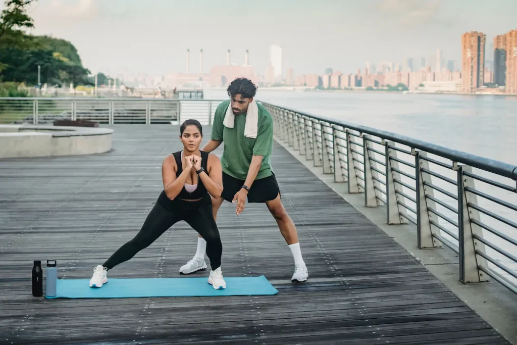 Mulher fazendo exercício ao ar livre com orientação de um personal trainer para ajudar na redução da gordura abdominal.
