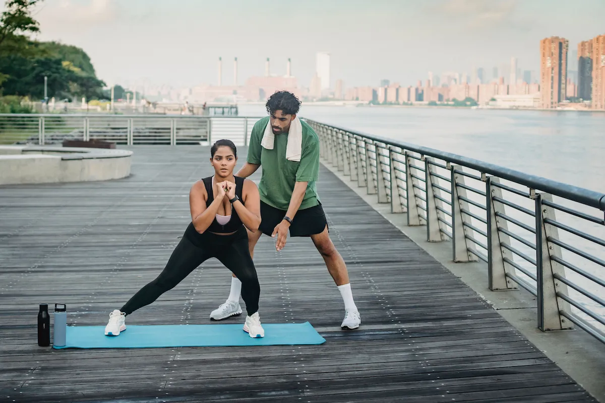 Mulher fazendo exercício ao ar livre com orientação de um personal trainer para ajudar na redução da gordura abdominal.